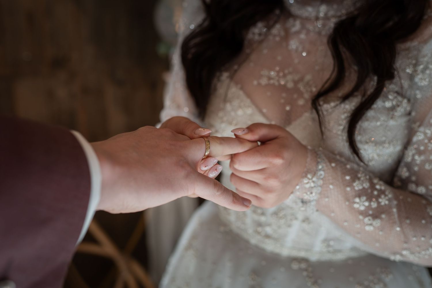 Groom placing a wedding ring on bride's finger during ceremony, bride wearing elegant lace dress.