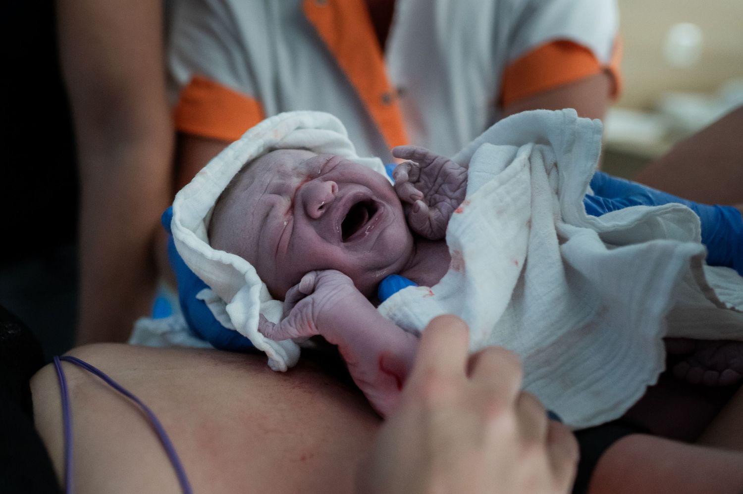 Newborn baby crying moments after birth wrapped in a hospital blanket.