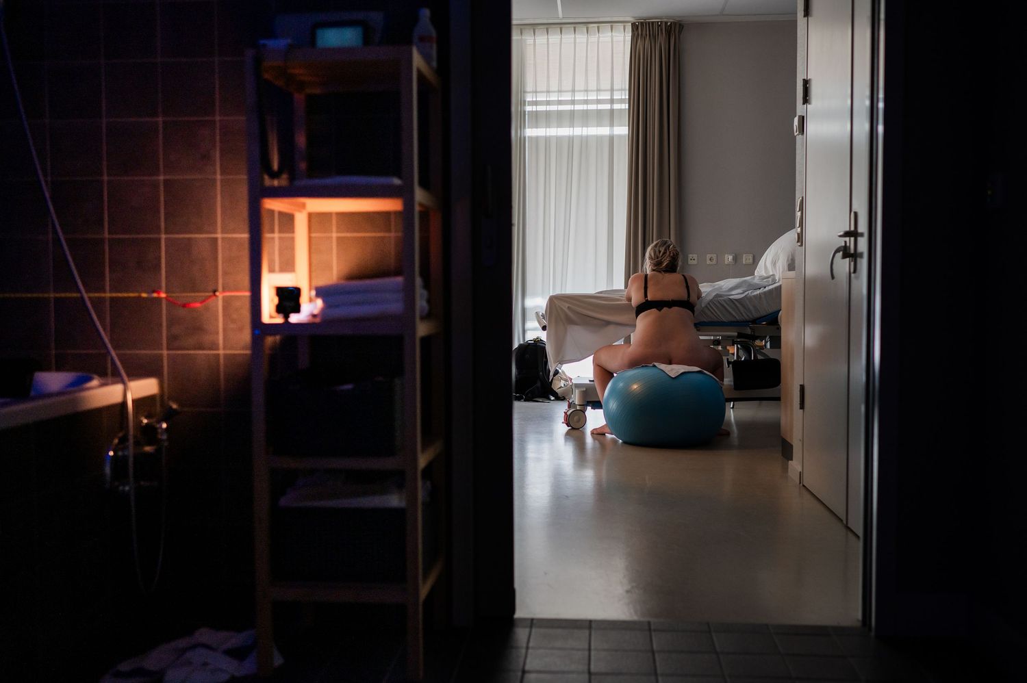 A woman in labor sits on a birthing ball in a dimly lit hospital room during active labor.