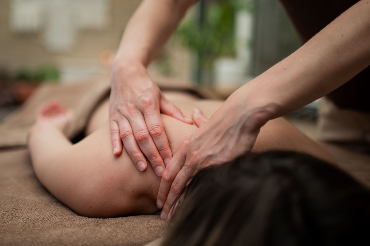 Professional massage therapist performing a relaxing back massage on a client lying on a spa treatment table.