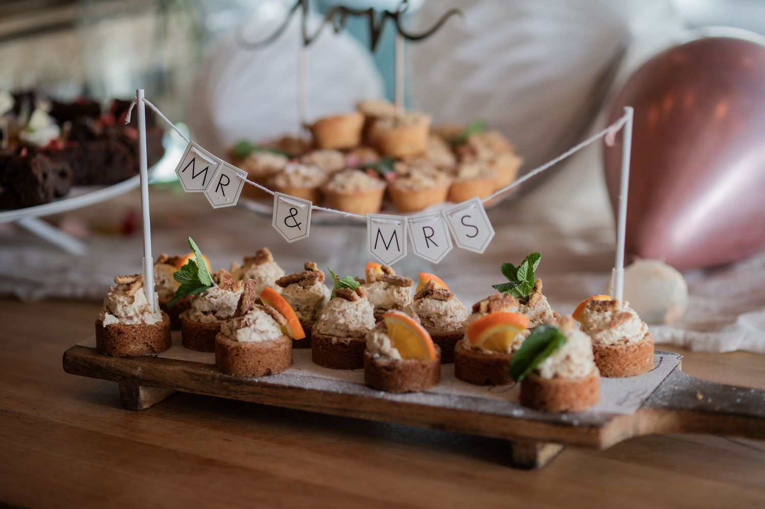 Wedding appetizers on wooden board with Mr & Mrs banner, featuring elegant bite-sized canapes at a rustic reception.