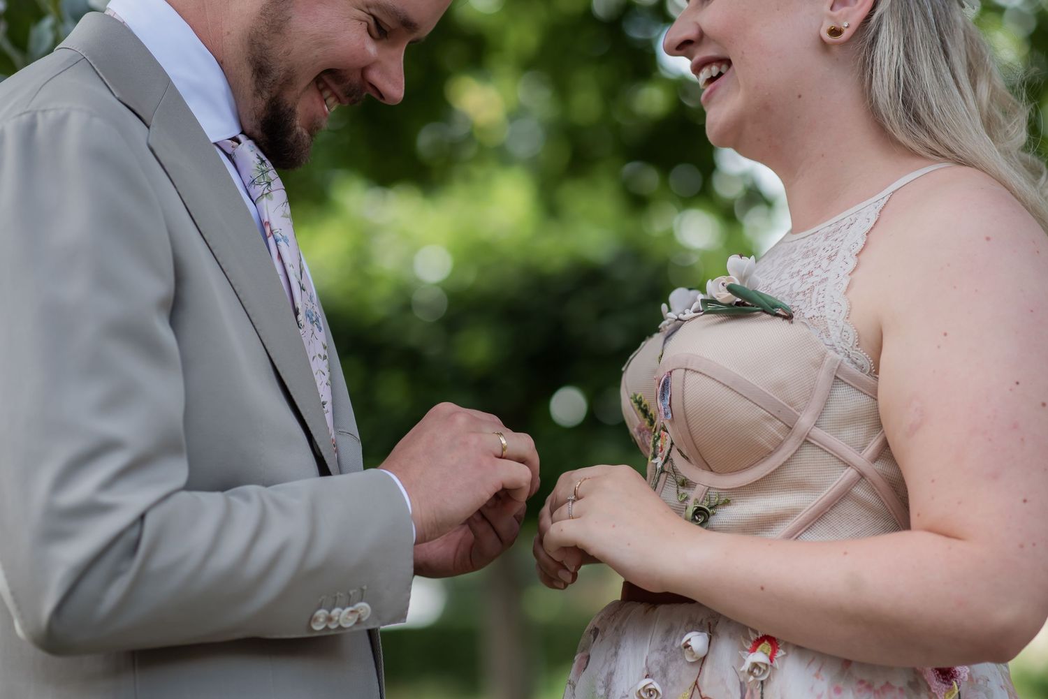 Groom placing wedding ring on bride's finger outdoors during romantic garden ceremony.