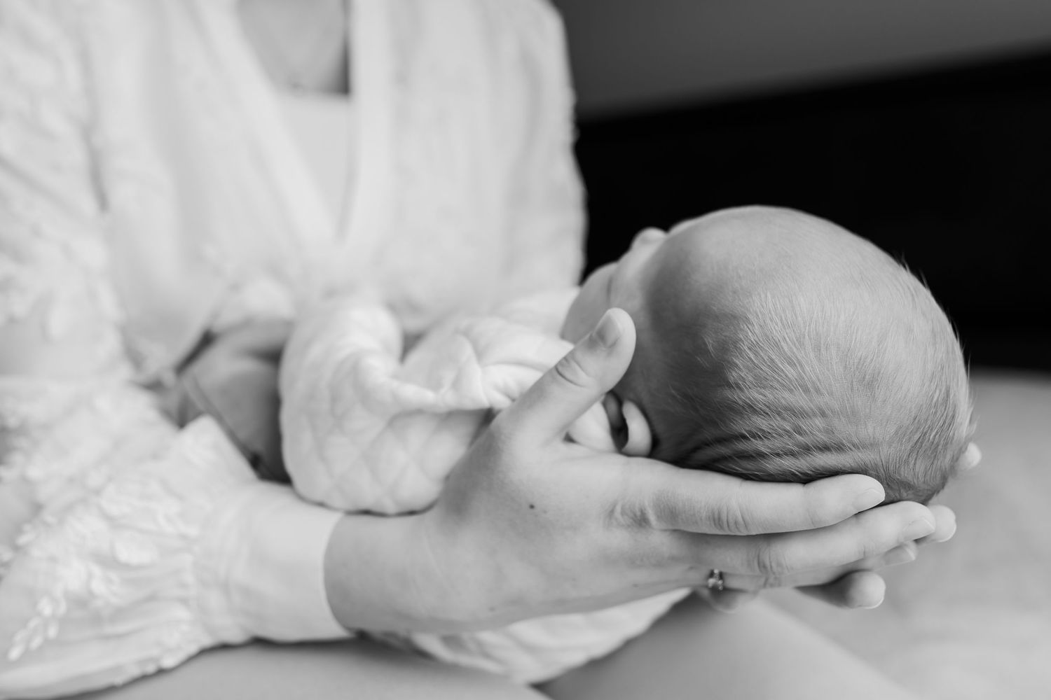 Black and white photo of a mother cradling her newborn baby's head gently in her hands.