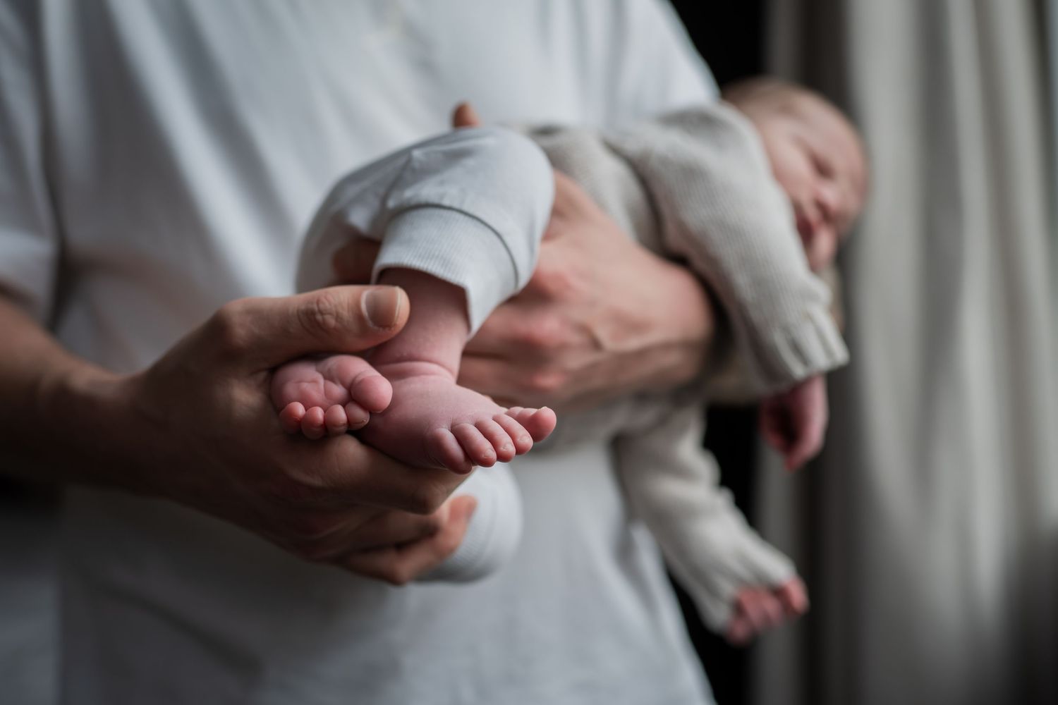 Parent gently holds a sleeping newborn baby's tiny feet in their hands indoors. Lelystad, Almere, Dronten, Flevoland