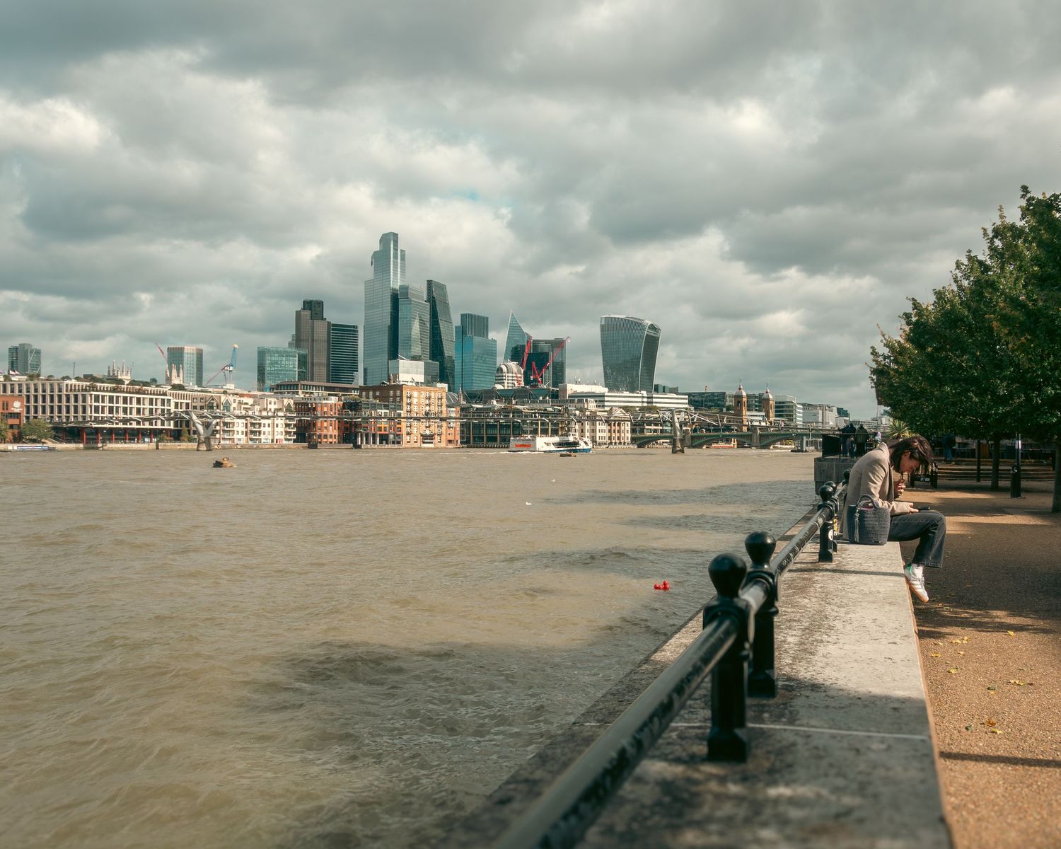 Donna seduta sul lungofiume del Tamigi guarda i grattacieli della City. Woman sitting by River Thames, London City skyline. MEvisual