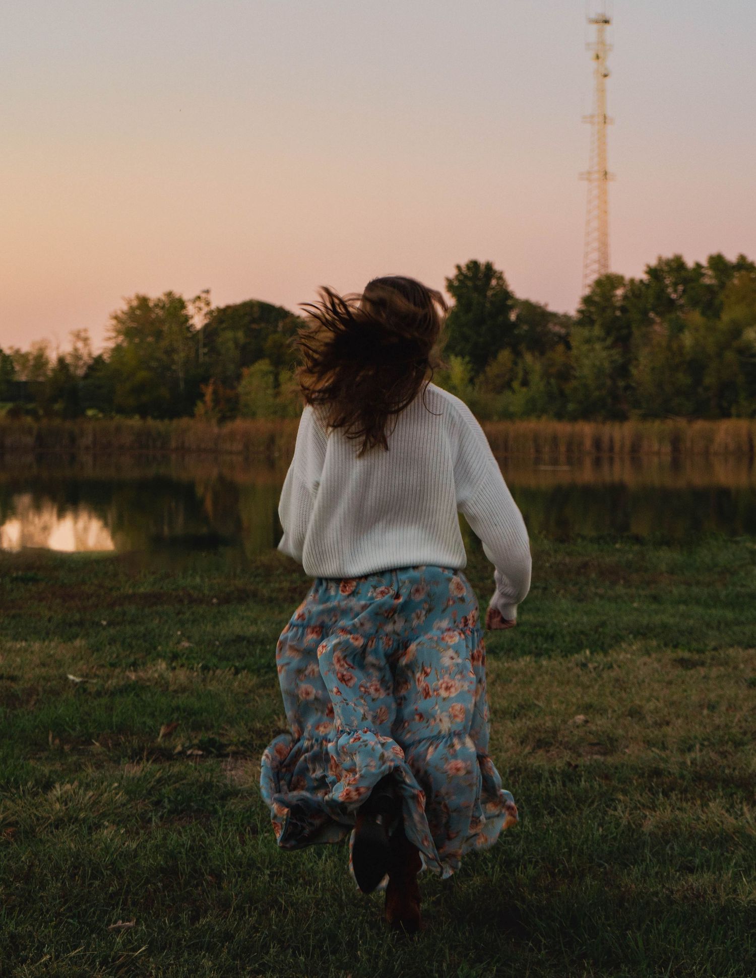 Woman in floral skirt running through green grass near a serene lake at sunset. Bethel Park, Shelby Renee Studios