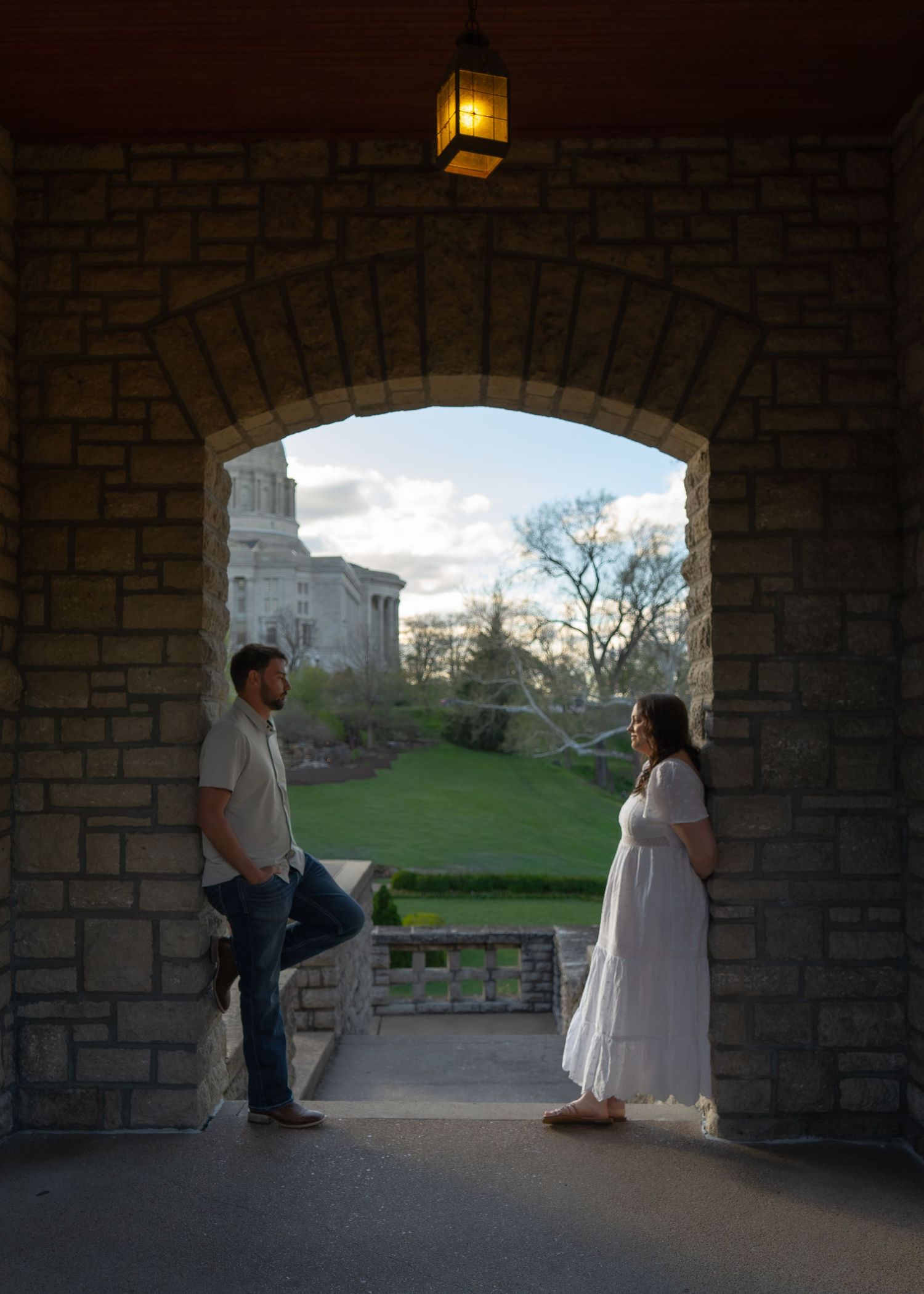 Couple standing under a stone archway with a lantern, facing each other in a romantic outdoor setting with a historic building.