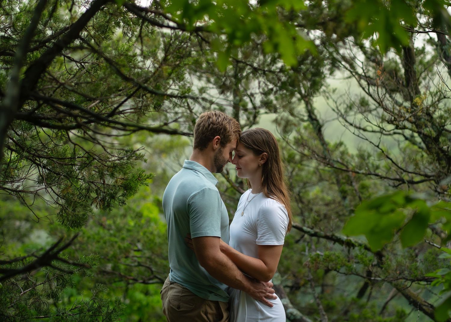 Romantic couple sharing an intimate moment surrounded by lush green forest foliage. Pinnacles Park Columbia MO Shelby Renee Studios