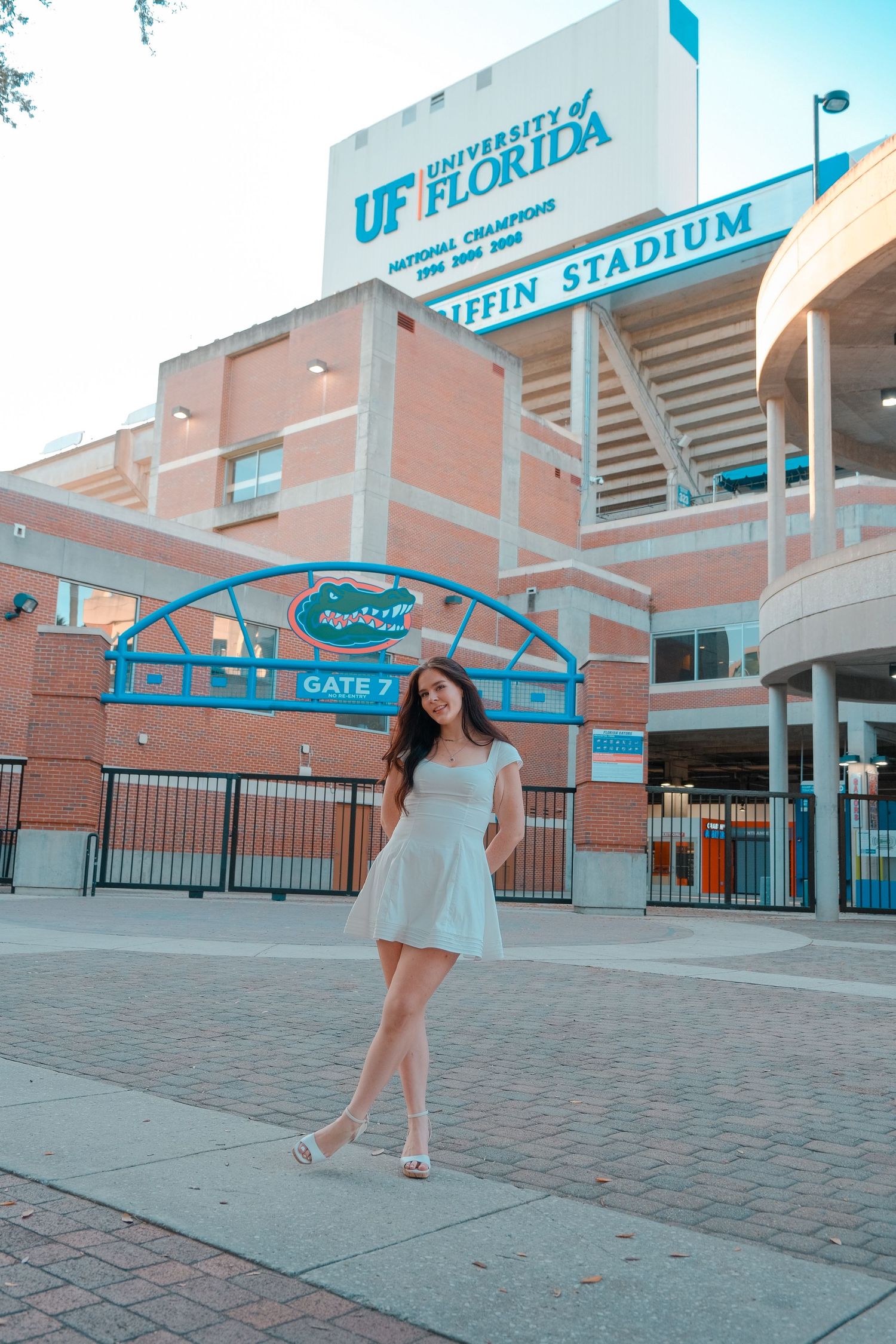 Young woman in white dress posing outside University of Florida Ben Hill Griffin Stadium gate.