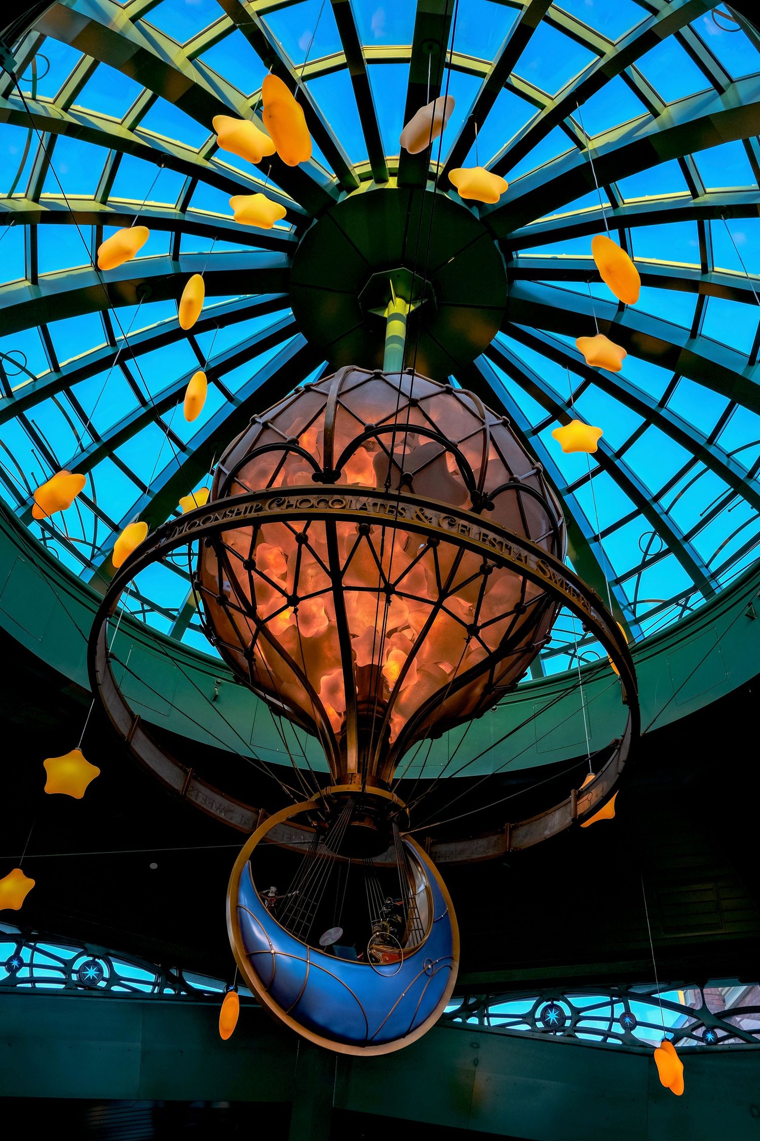 Ornate hot air balloon chandelier hangs beneath a stunning blue glass dome ceiling with yellow star decorations.
