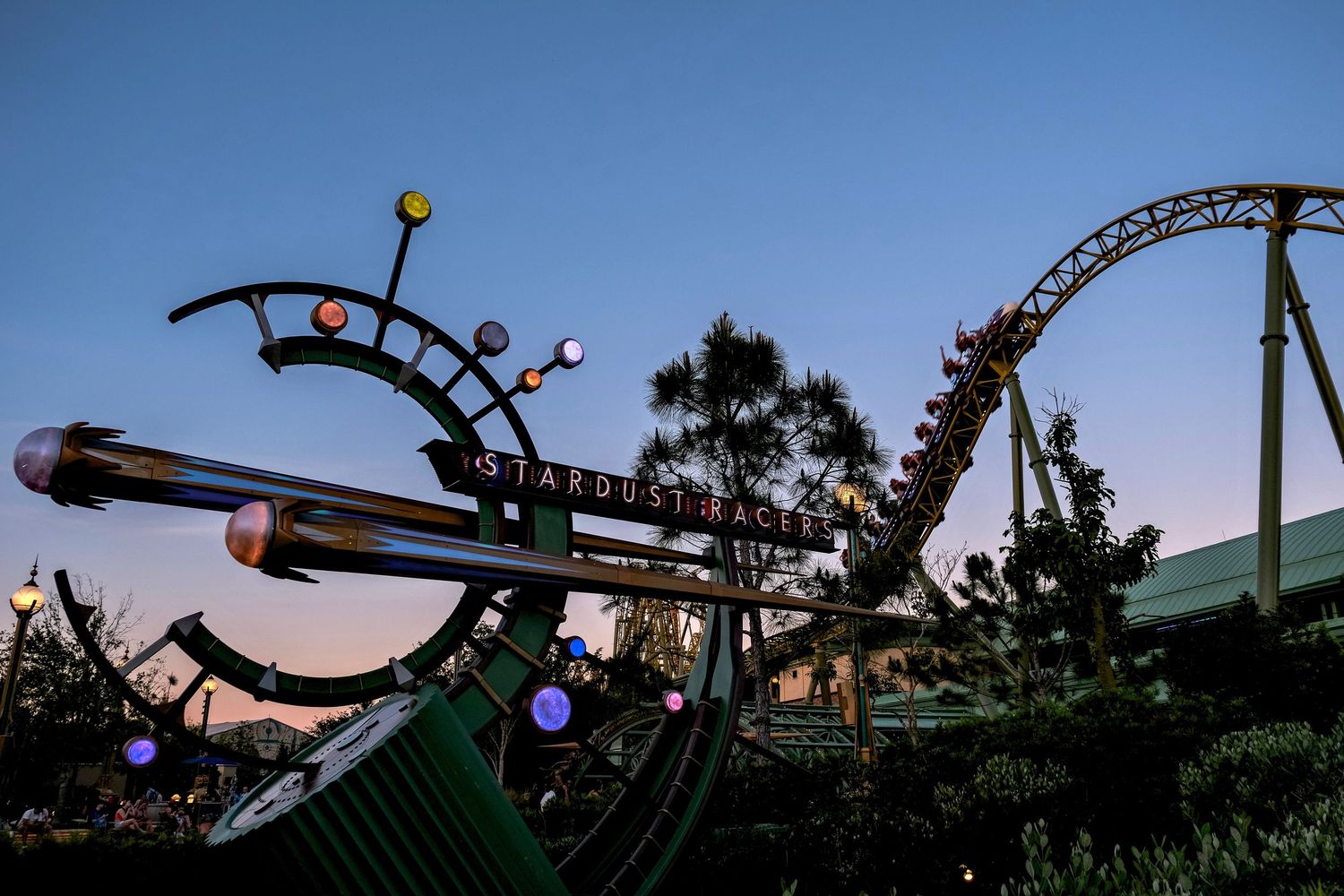 Stardust sign at dusk with roller coaster and colorful planet decorations at an amusement park.