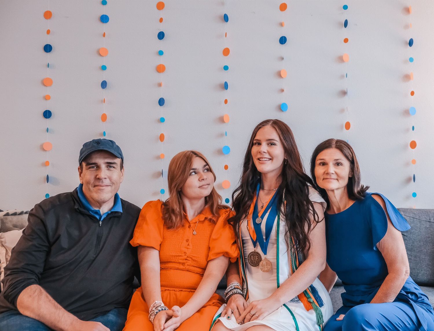 Family of four smiling together at a celebration, decorated with colorful orange and blue circle garlands in the background.