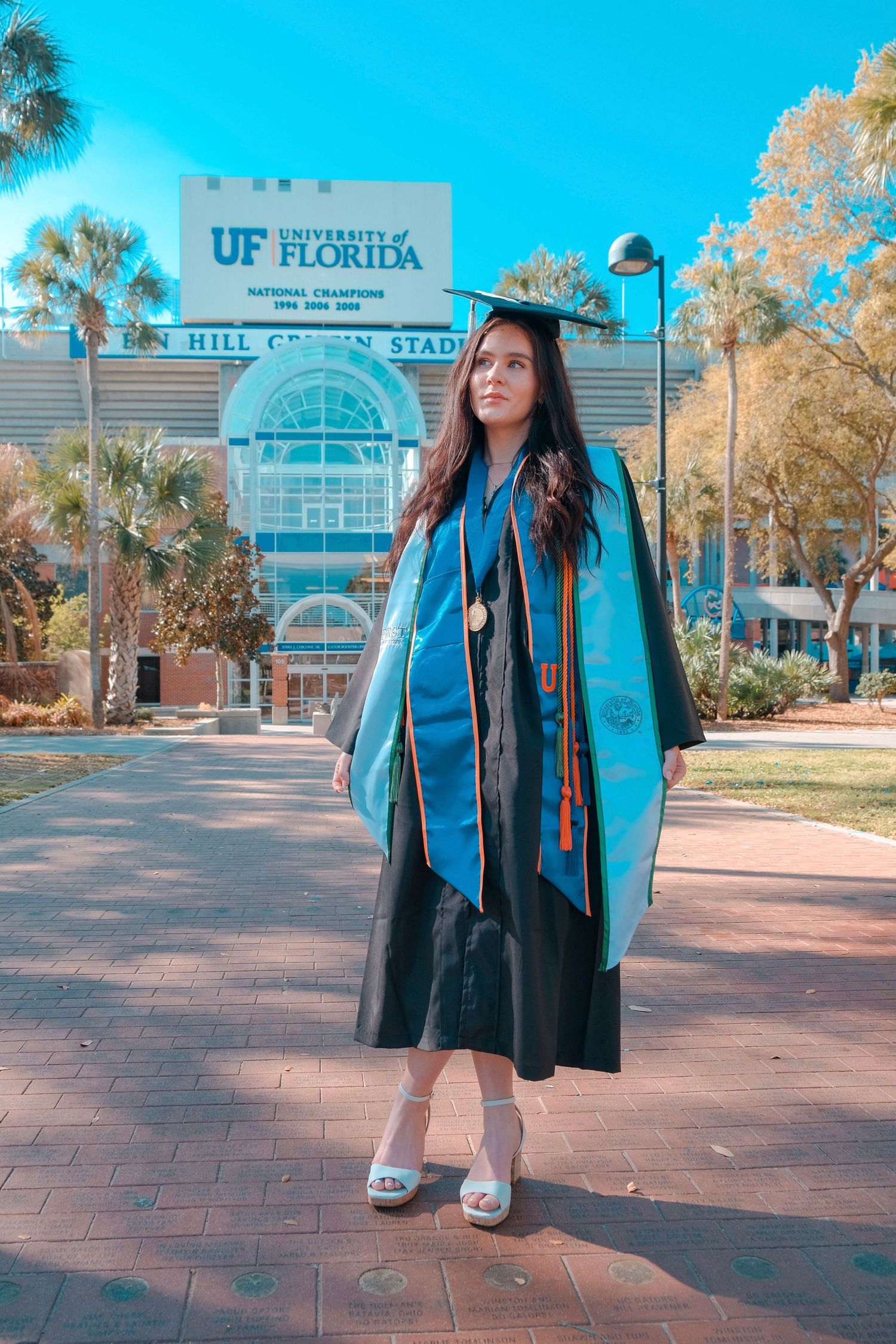 University of Florida graduate poses in cap and gown outside Ben Hill Griffin Stadium on a sunny day.