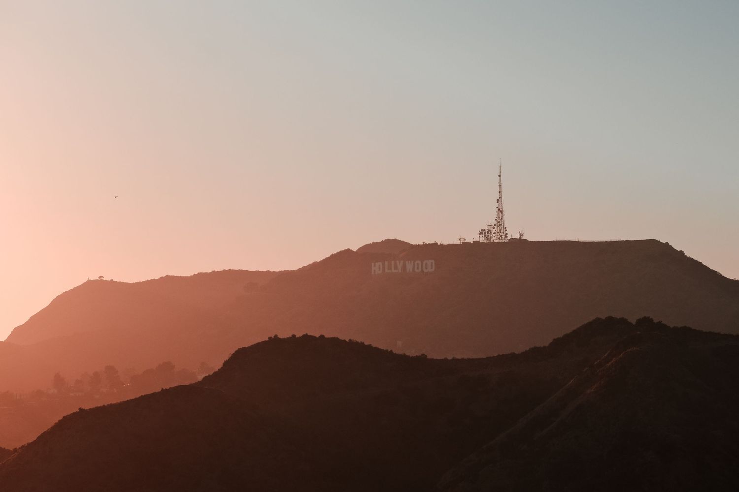 Aerial sunset view of the Hollywood Sign on a hilltop in Los Angeles, CA, with warm orange hues.