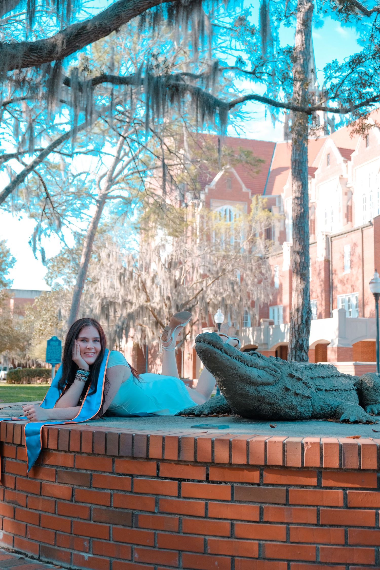 Young woman in blue dress posing with a bronze alligator statue on a brick wall at University of Florida campus.