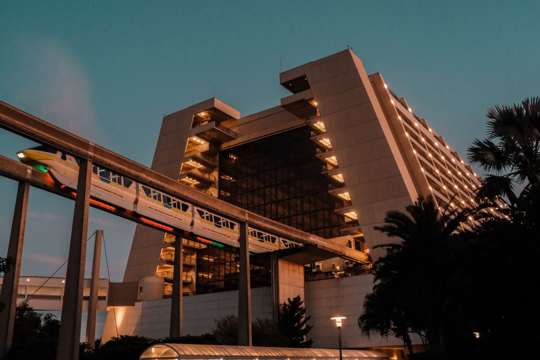Modern hotel building photographed at dusk with warm golden lights illuminating balconies against a teal evening sky.