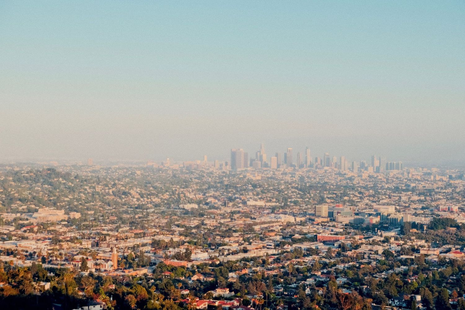 Aerial panoramic view of Los Angeles skyline with urban sprawl and hazy smog under clear blue sky.