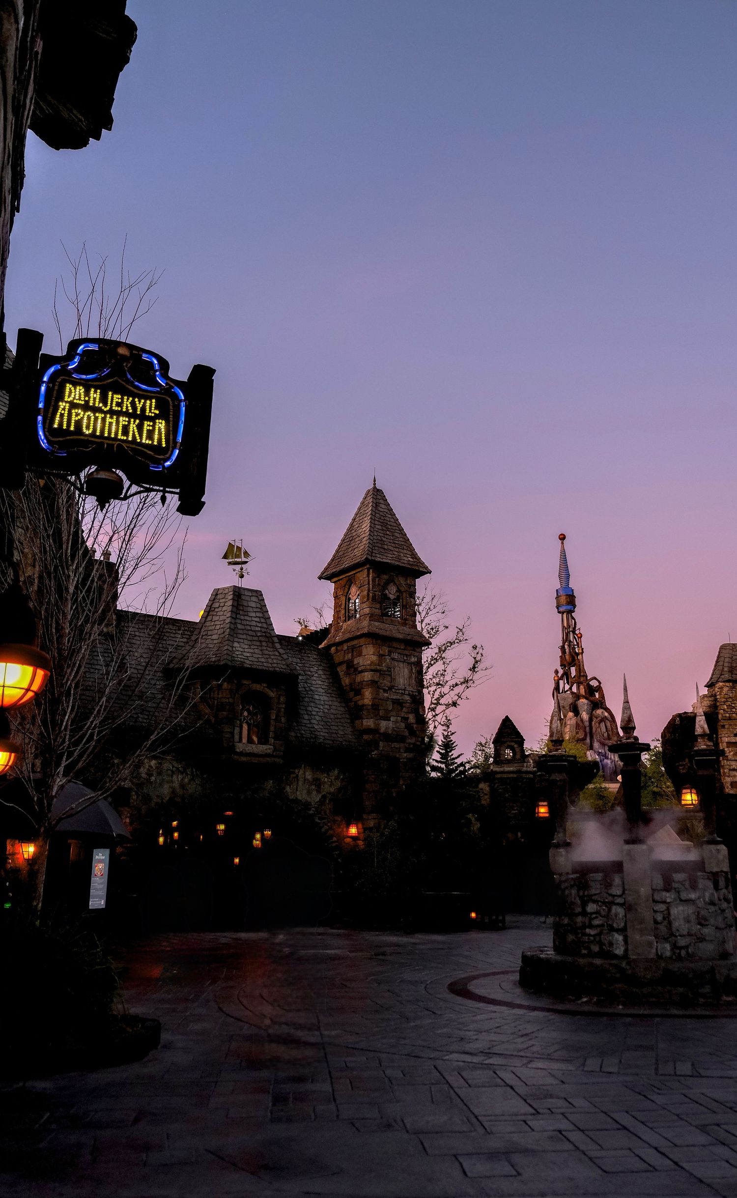 Twilight view of Dr. H. Jekyll Apotheke sign at a themed park with gothic architecture and glowing lanterns.