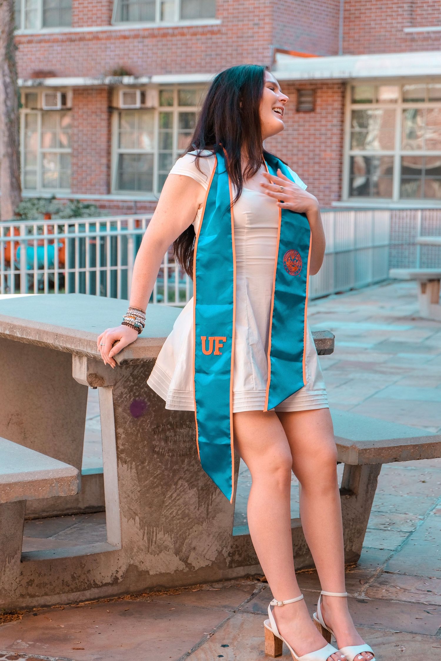 Laughing UF graduate wearing teal graduation stole poses outdoors on University of Florida campus.
