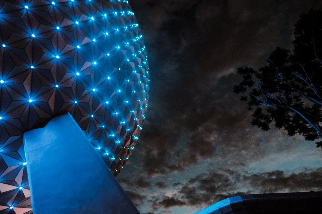 Illuminated geodesic dome structure glowing with blue LED lights against a dramatic cloudy night sky.