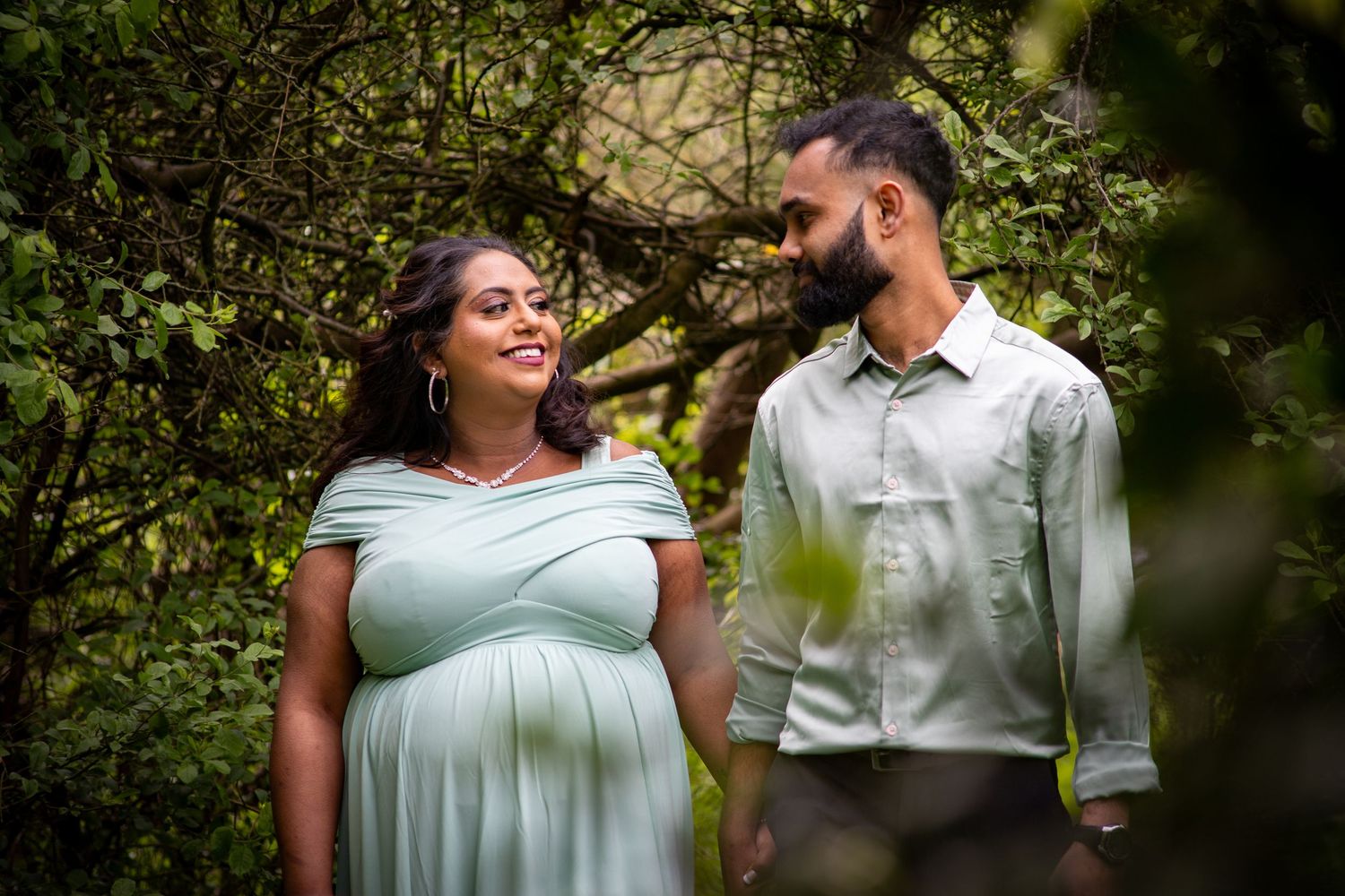 Couple smiling at each other during outdoor maternity photoshoot with natural lighting in London, UK