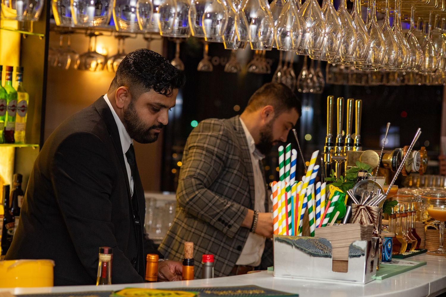 Bartenders preparing drinks behind bar during restaurant opening event in Heathrow, London, UK