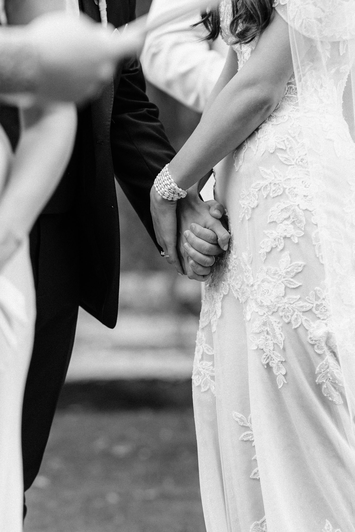 Black and white photo of bride and groom holding hands during wedding ceremony.