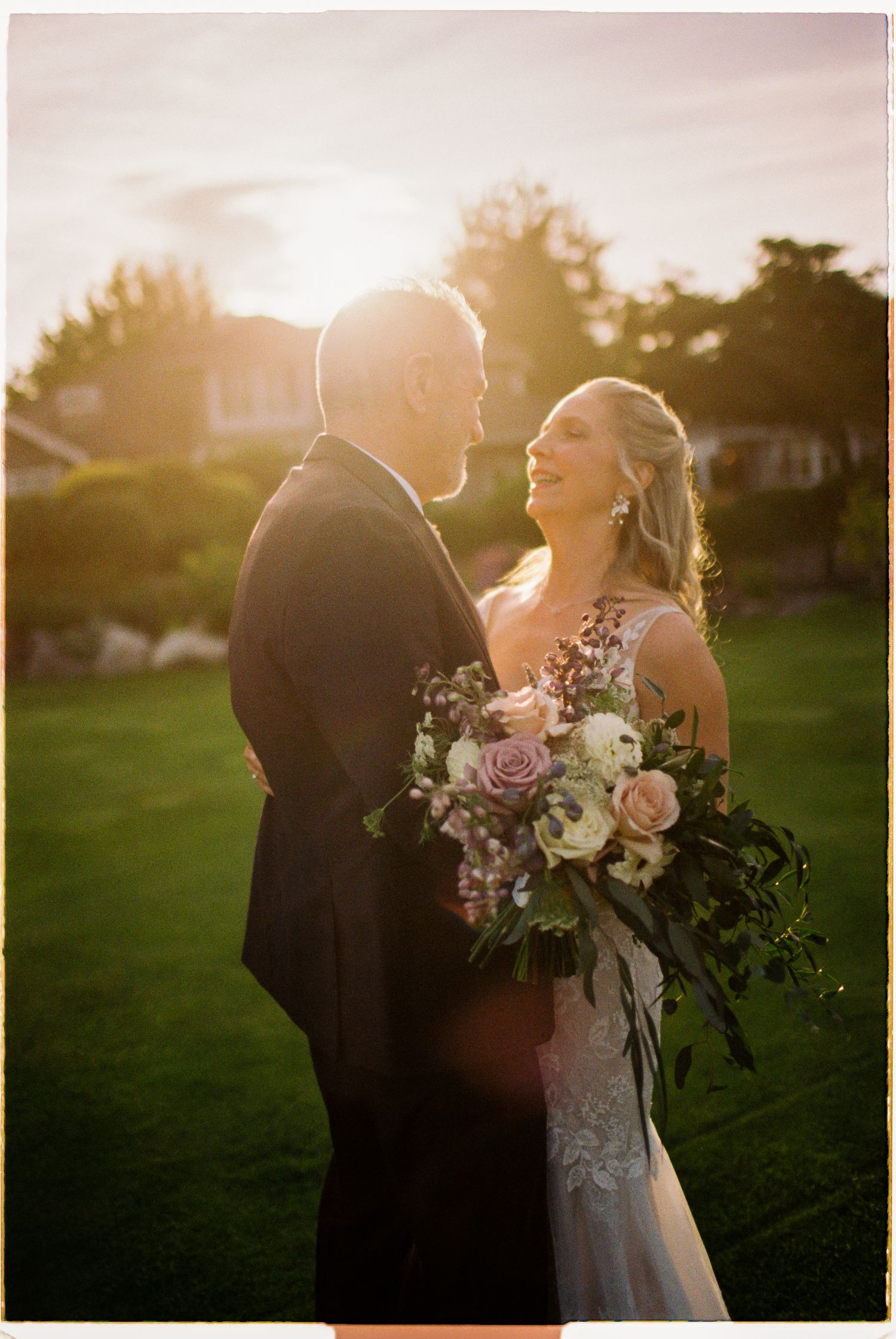 Bride and groom sharing a romantic moment in golden sunset light, bride holding a lush pink and white bouquet.