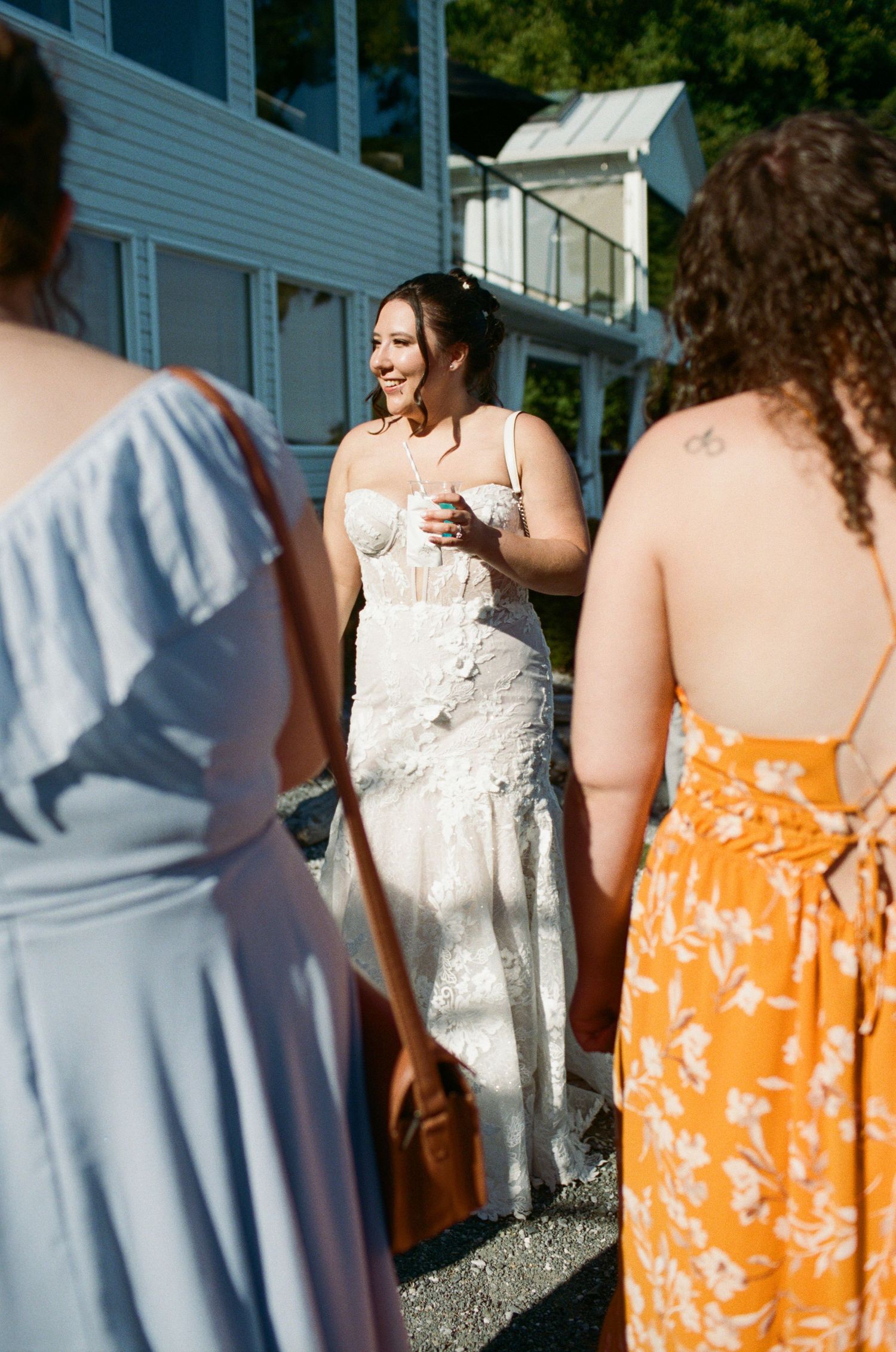 Smiling bride in lace wedding gown chatting with guests in colorful dresses at outdoor wedding.