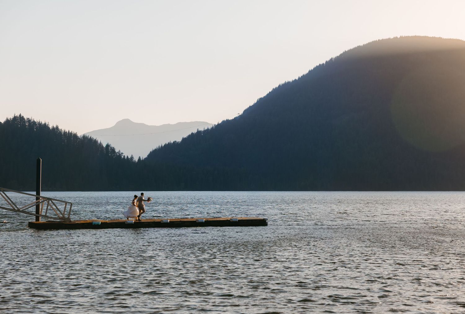 Couple standing on a floating dock surrounded by a serene mountain lake at dusk.