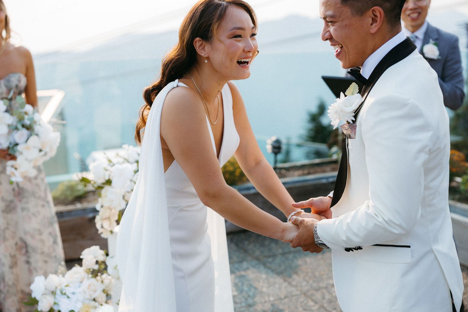Joyful bride and groom holding hands and laughing during outdoor wedding ceremony with mountain views.