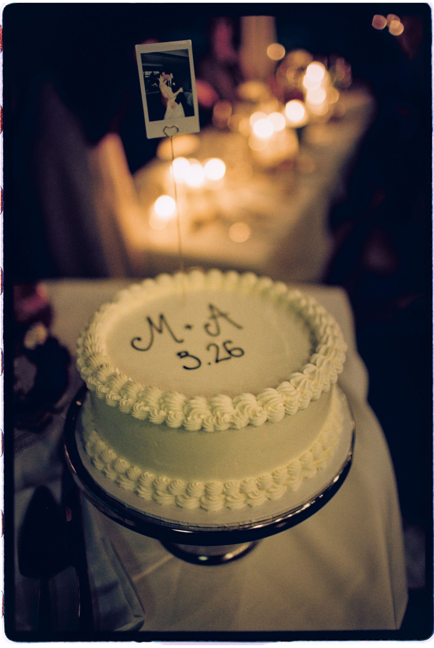 Simple white wedding cake inscribed with M+A 3.26 displayed on elegant cake stand.