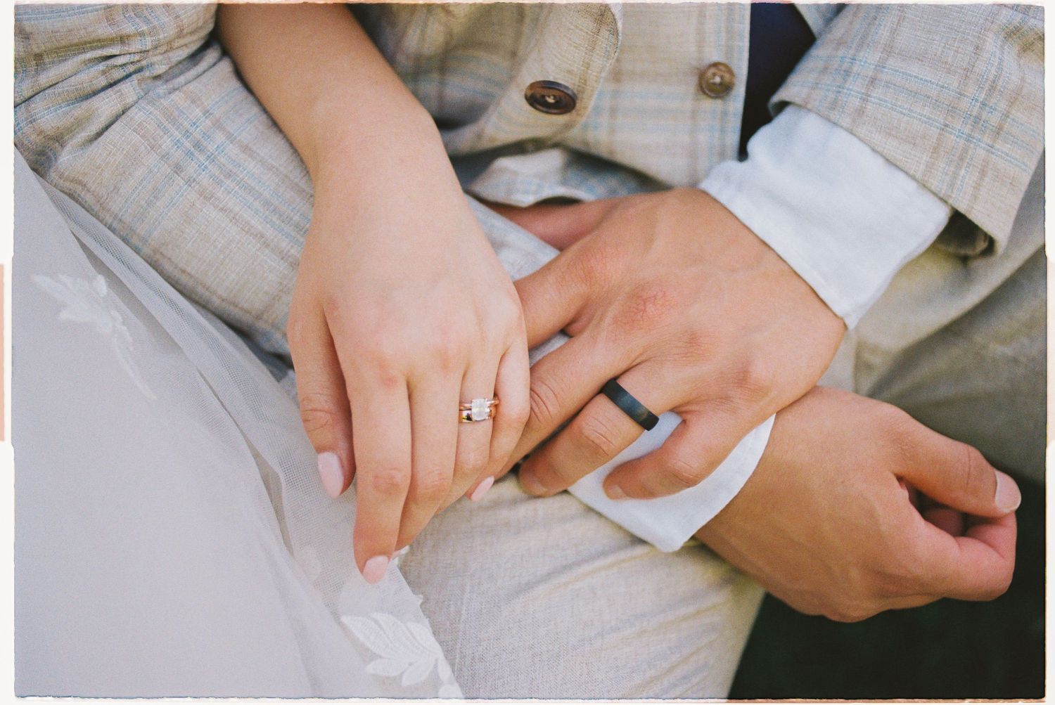Close-up of bride and groom holding hands showing diamond engagement ring and silver wedding band at wedding.