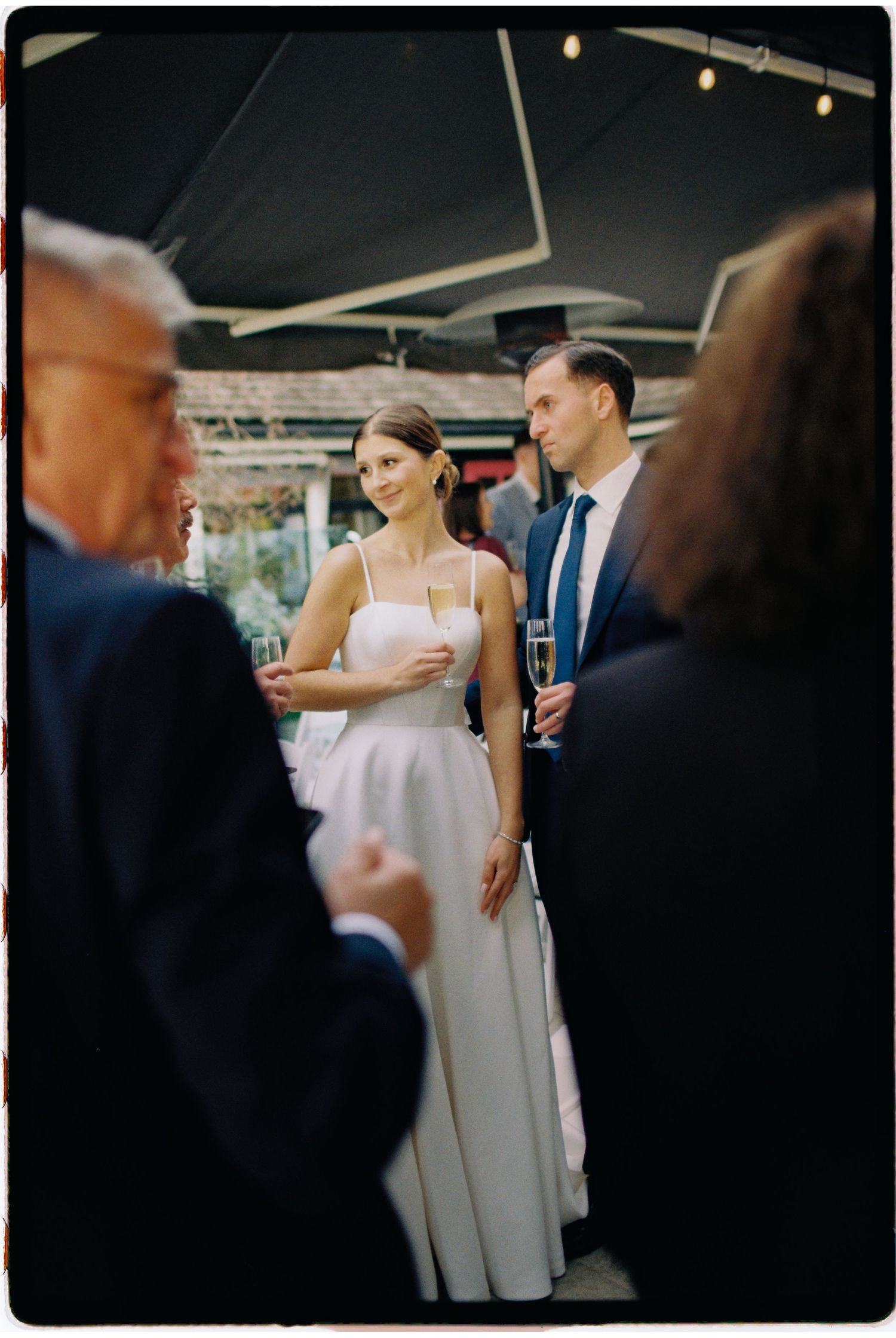 Bride in white gown holding champagne while conversing with guests at wedding reception.