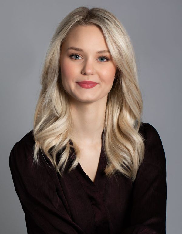 Professional blonde woman in black blouse with red lips against gray background.
