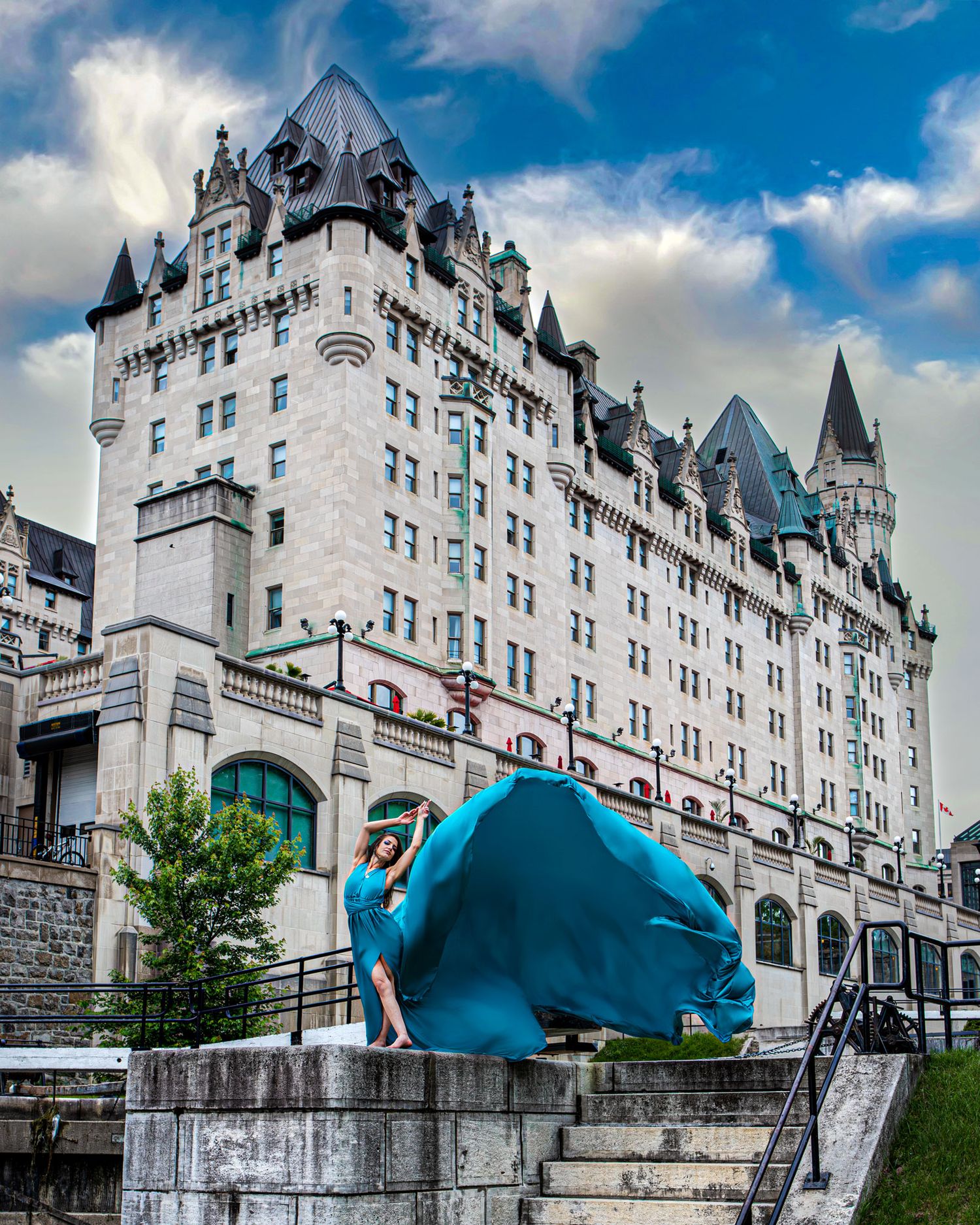 Woman in flowing teal gown poses on stone steps before Chateau Laurier castle hotel Ottawa. Ottawa flying dress luxury photography