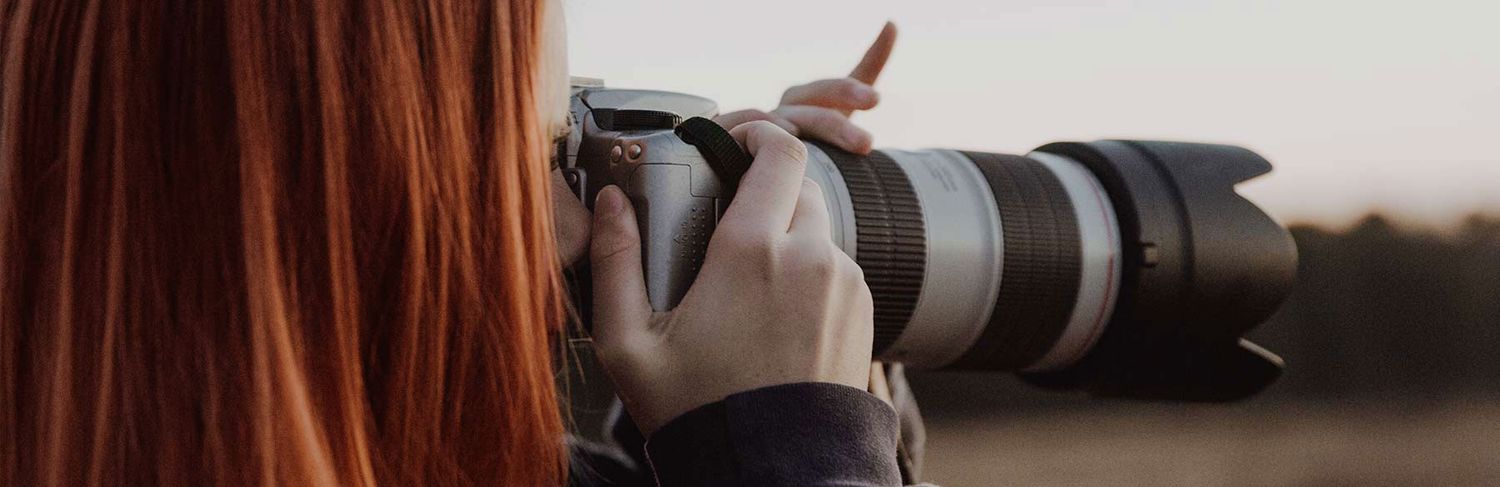 Female photographer with red hair shooting with a professional camera and telephoto lens.