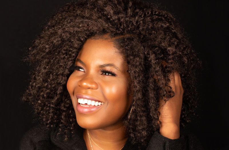 Smiling Black woman with voluminous natural curly hair wearing black jacket in professional portrait photography.
