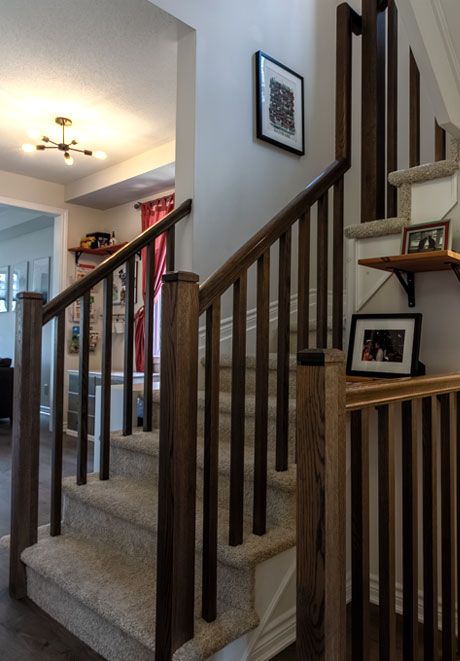 Elegant home staircase with dark wood banisters, carpeted steps, framed photos on wall, and decorative shelf with picture frames.