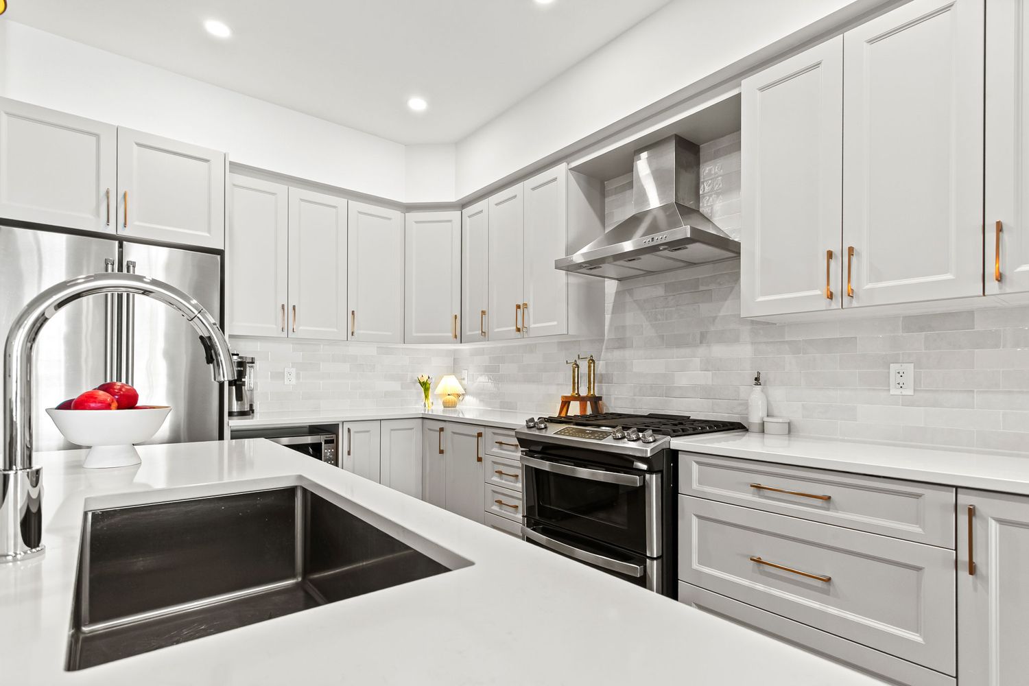 Professional real estate photography of Sleek gray kitchen with quartz countertops, wall-mount range hood, and copper hardware.