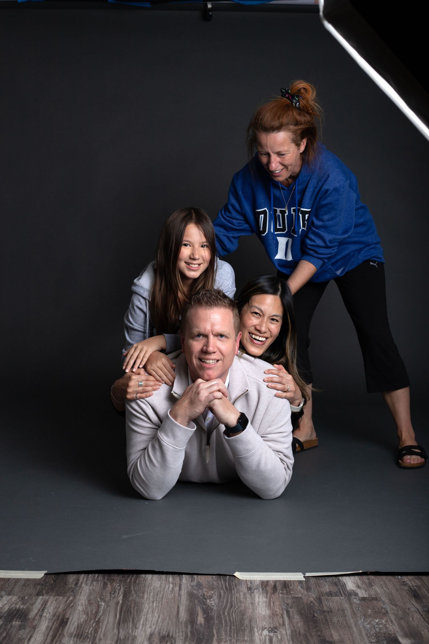 Fun family studio portrait with four people stacking and hugging in front of dark backdrop. behind the scenes BTS