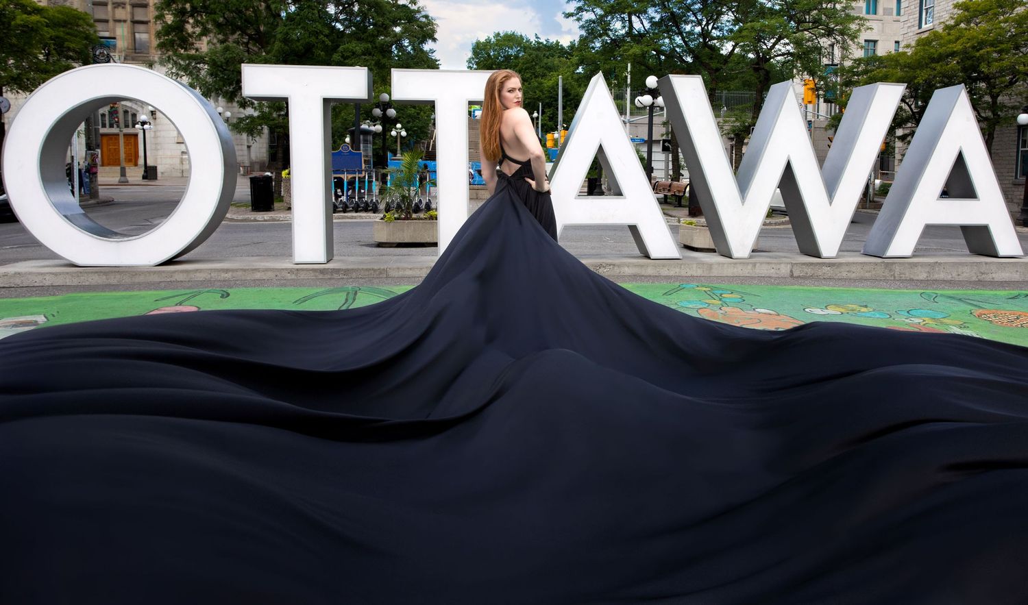 Woman in flowing black dress poses dramatically before the iconic Ottawa sign downtown. Ottawa flying dress photography. Byword market