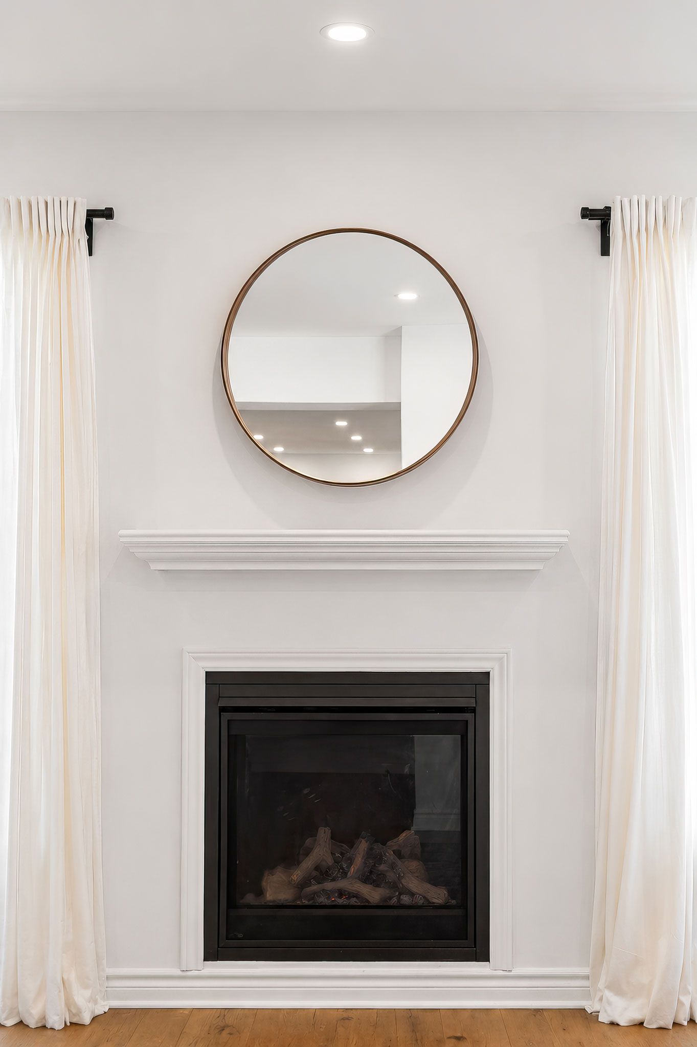 Professional real estate photography of Elegant white fireplace round copper mirror above mantel, flanked by white curtains