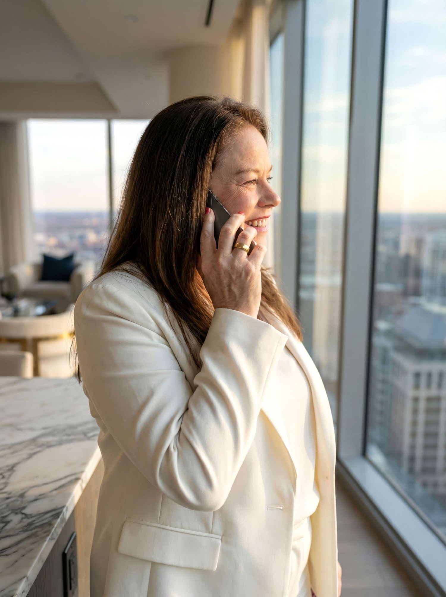 Businesswoman in white blazer smiling during phone call with city skyline view.