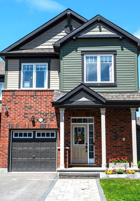 Modern two-story brick and green siding family home with attached garage and landscaped front yard.