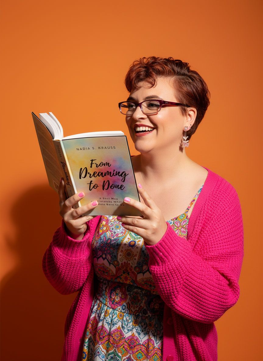 Smiling woman with short red hair holding From Dreaming to Done book on orange background.