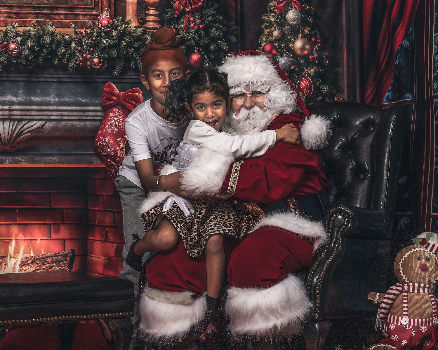 Two children hugging Santa Claus beside a glowing fireplace in a festive Christmas setting.