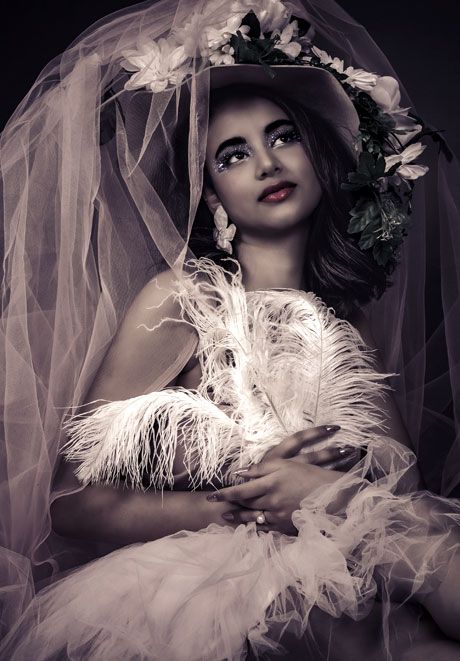 Elegant woman in white feather dress and floral veil in artistic bridal portrait.