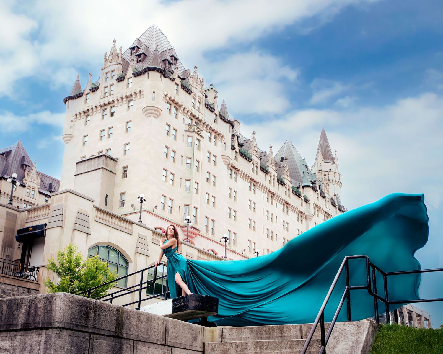 Woman in billowing teal dress poses on steps with Chateau Laurier Ottawa backdrop. Ottawa flying dress luxury photography