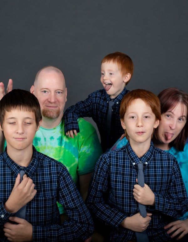 Playful redhead family making silly faces during a fun studio portrait session with matching blue plaid shirts.